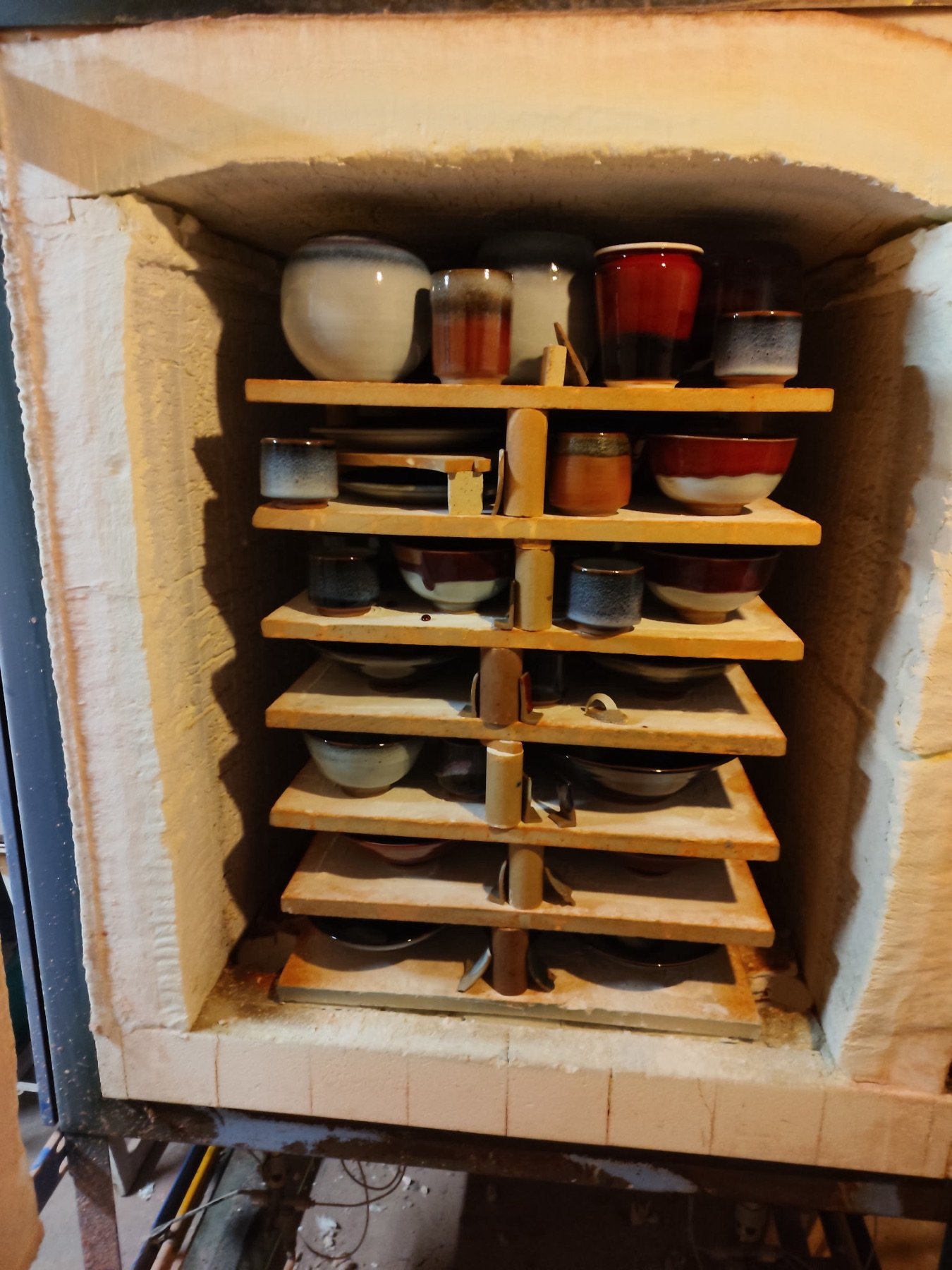 Le four de l’atelier, porte ouverte, chargé de pièces émaillées sur plusieurs étagères
