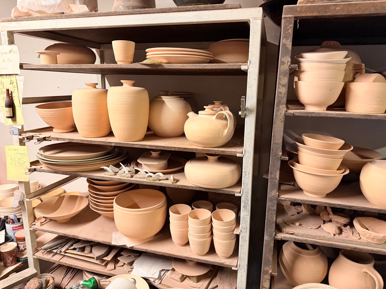 Étagères de l’atelier chargées de pièces nues : vases, pots, bols et théière