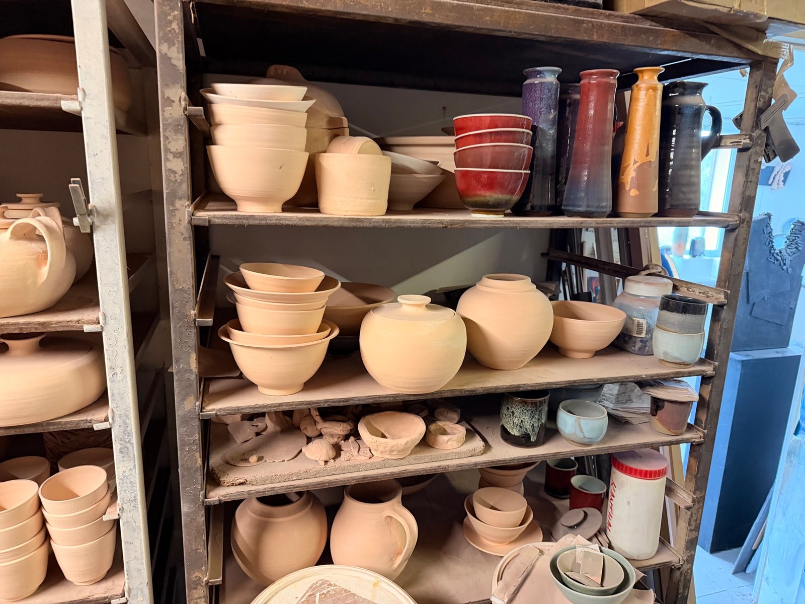 Autres étagères de l’atelier, avec des bols et des pots nus et quelques vases colorés