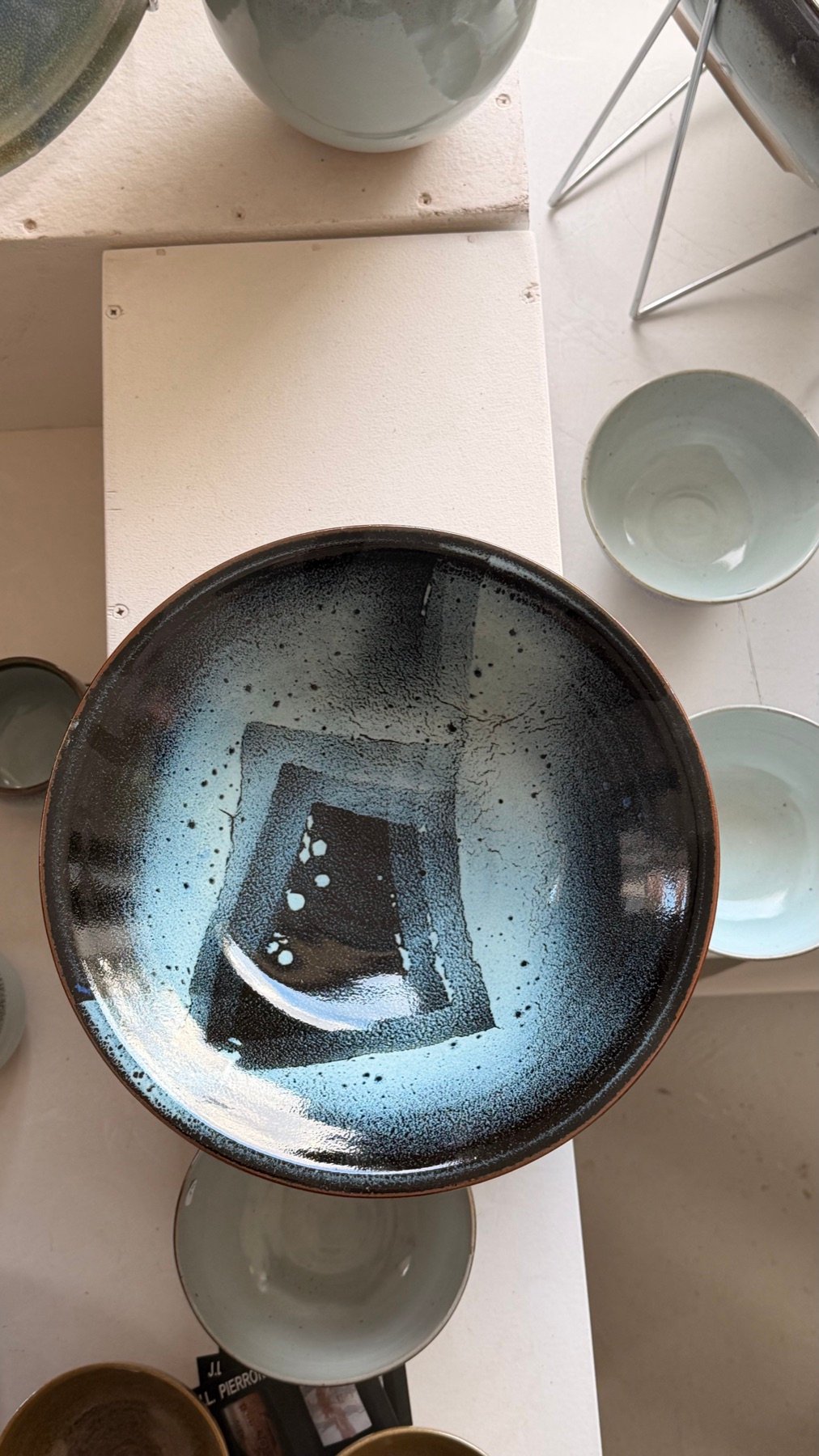 Grande assiette creuse à la glaçure bleue et noire, vue de dessus, entourée de bols
